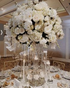 a tall vase filled with lots of white flowers on top of a table covered in candles