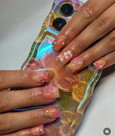 a woman's hands with pink and yellow flowers on her nails holding a phone case