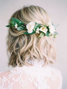 the back of a woman's head with white flowers in her hair and greenery