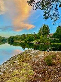 a lake that is surrounded by trees and grass in the foreground with a sky filled with clouds