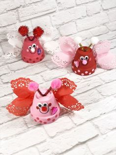 three little red and pink angel ornaments on a white brick wall, one is wearing a tiara