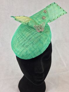 A pretty pillbox hat made from mint green Sinamay layered with pale yellow Sinamay to give an unusual patterned effect. It is decorated with a bow towards the back which is itself decorated with filigree butterflies of graduating sizes and toning green diamanté crystals along the edge of the bow.  The hat is attached to the head with elastic which makes it easy and comfortable to wear.  It is slightly deeper at the back than the front and measures 16cms x 17cms. Green Evening Hat, Green Evening Fascinator Hat, Green Headpiece For Church And Royal Ascot, Green Pinched Crown Headpiece For Parties, Green Headpieces For Church And Kentucky Derby, Green Top Hat For Kentucky Derby Evening, Green Adjustable Formal Hats, Adjustable Green Mini Hat For Wedding, Adjustable Green Costume Hats And Headpieces As Gift