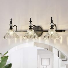 three light bathroom fixture with clear glass shades and black metal frame, on white wall