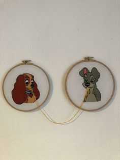 two embroidery hoop paintings with lady and the tramp characters on them, hanging on a wall