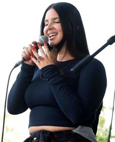 a woman singing into a microphone while standing in front of a microphone with her hands on her hips