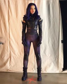 a woman with purple hair and black catsuits standing in front of a white backdrop