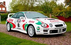 a white car parked on top of a gravel road next to a lush green field