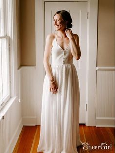 a woman standing in front of a window wearing a white dress and smiling at the camera