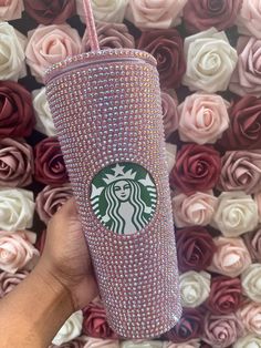 a hand holding a pink starbucks cup in front of roses