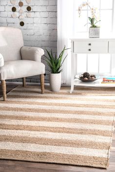 a living room with a chair, rug and potted plant on the floor in front of a brick wall