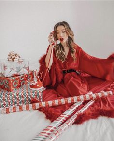 a woman in a red dress is sitting on a bed and talking on the phone