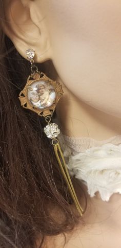 "These striking angel assemblage earrings are so much fun!  The focal point of these gorgeous long earrings are vintage brass settings displying adorable cherub / angel pictures. The back is finished with a genuine leather patch. The long tassel is made with large sparkling rhinestone ball beads and pretty vintage brass snake chain. These striking dangle earrings drop 4 3/4\" from the Swarovski rhinestone posts. Our upcycled jewelry will make a beautiful gift for Christmas, a birthday or an anni Vintage Earrings With Dangling Charms As Gift, Vintage Earrings With Dangling Charms For Gift, Vintage Cherub, Assemblage Earrings, Found Object Jewelry, Duster Earrings, Cherub Angel, Assemblage Jewelry, Angel Pictures