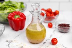 a glass bottle filled with olive dressing next to bowls of tomatoes and lettuce