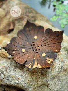 a brown metal flower sitting on top of a rock next to a body of water