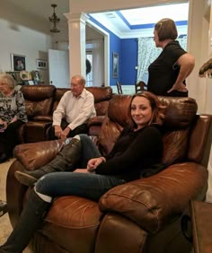 three people sitting on brown leather couches in a living room with two women and one man