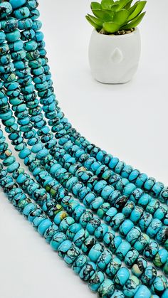 several strands of turquoise beads next to a potted plant on a white table top