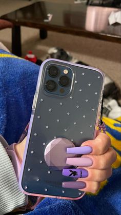 a woman holding up her phone case with purple nails and heart shaped stickers on it