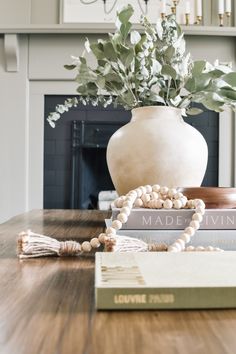 a vase with flowers and beads sitting on top of a wooden table next to a book