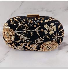 a black and gold embroidered clutch bag on a marble countertop with skulls, flowers, and leaves