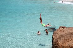 a man diving into the ocean with his feet in the water and people swimming nearby