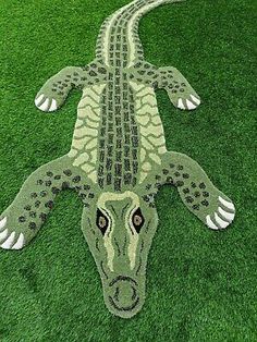 an animal made out of green grass on top of the ground with its eyes open