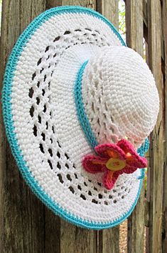 a crocheted hat is hanging on a wooden fence with a flower in the center