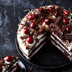 a chocolate cake with cherries on top and one slice cut out from the cake