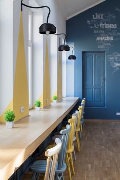 a long table with yellow and blue chairs in front of a chalkboard on the wall