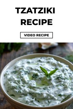 a bowl filled with white sauce and garnished with green leafy herbs, on top of a wooden table