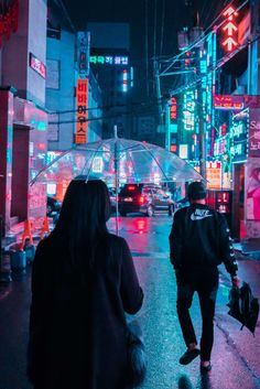 two people walking down the street in the rain with umbrellas over their heads at night