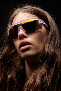 a woman with long hair wearing sunglasses and looking off to the side, in front of a black background