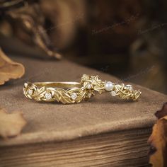 two gold rings with pearls on top of a wooden table next to an oak leaf