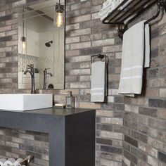 a bathroom with brick walls and a white sink in the middle, surrounded by towels