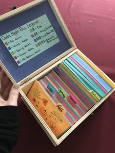 a person holding an open wooden box with writing on it and colorful papers in it