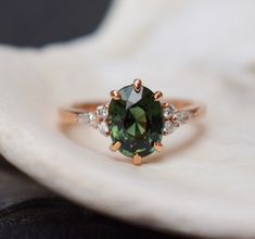 a green and white diamond ring sitting on top of a white flower petal piece