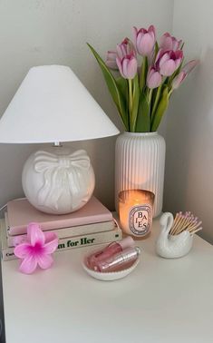 a white table topped with a lamp next to a book and pink tulips