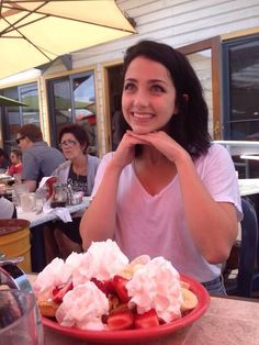 a woman sitting at a table in front of a plate of food with whipped cream and fruit