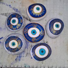 four blue and white painted rocks with an evil eye design on the top, sitting on a piece of wood