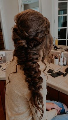 a woman with long hair sitting in front of a bathroom sink and looking into the mirror