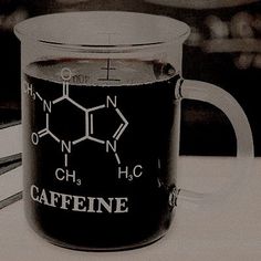 a glass coffee mug with caffeine written on the front and side, sitting next to some books