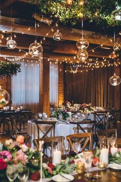 a dining room filled with lots of tables covered in white table cloths and hanging lights