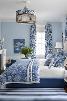 a bedroom with blue and white bedding, curtains, chandelier and fireplace