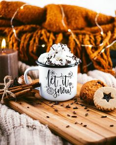 a mug with whipped cream and cookies on a cutting board next to some cinnamons