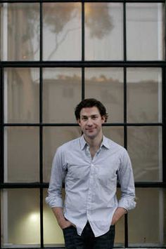 a man standing in front of a window with his hands in his pockets and looking at the camera