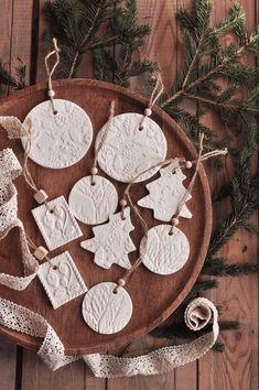 some ornaments are sitting on a wooden plate next to a ribbon and pine tree branch