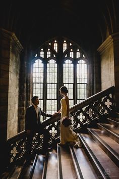 a bride and groom walking down the stairs in an old building with stained glass windows