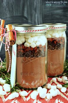 three mason jars filled with hot chocolate and marshmallows on top of a table