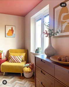 a living room filled with furniture and a yellow chair next to a wooden dresser under a window