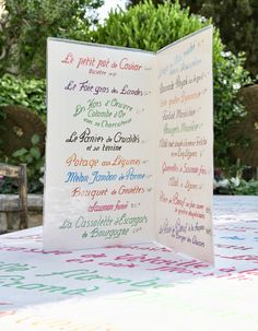 an open book sitting on top of a table covered in colorful writing and trees behind it