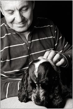 a black and white photo of a man petting a dog